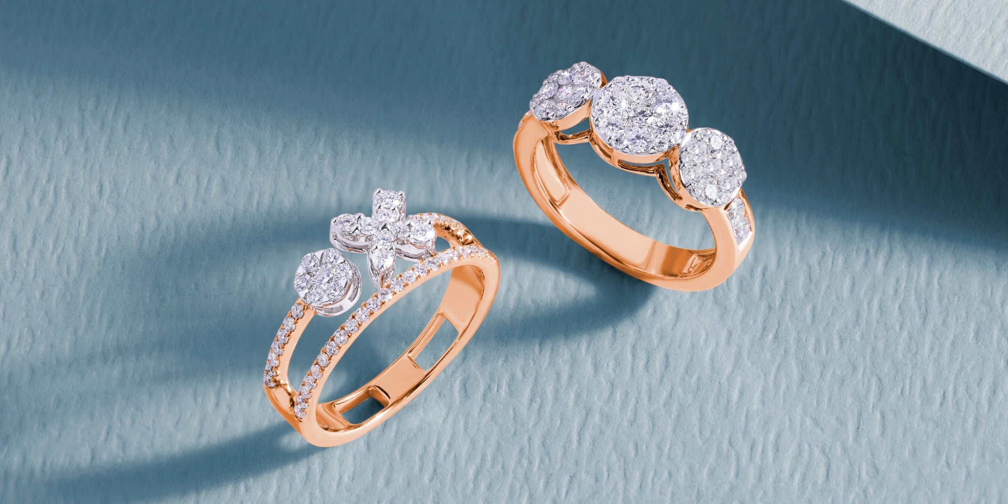 Two rose gold diamond rings on a light blue background
